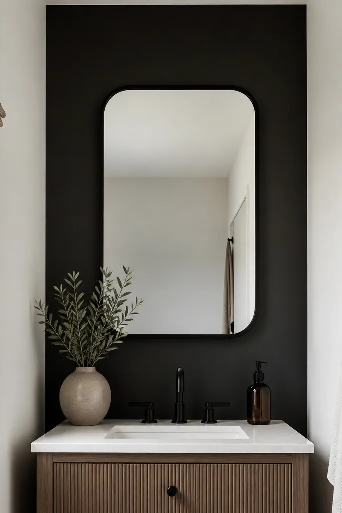 Behind a small vanity, there is a matte black removable wall panel. The panel is smooth and flat, with clean edges. A black framed mirror hangs centered above it, and the rest of the bathroom walls are white.